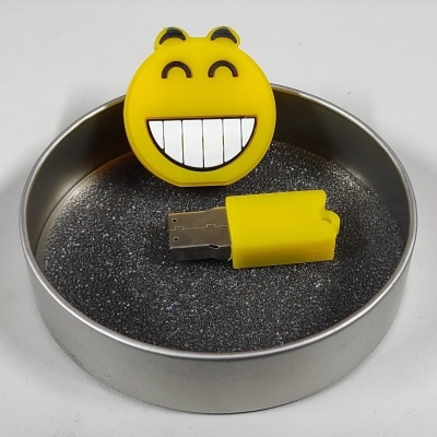Pen USB amarelo em forma de emoji sorridente dentro de caixa metálica redonda