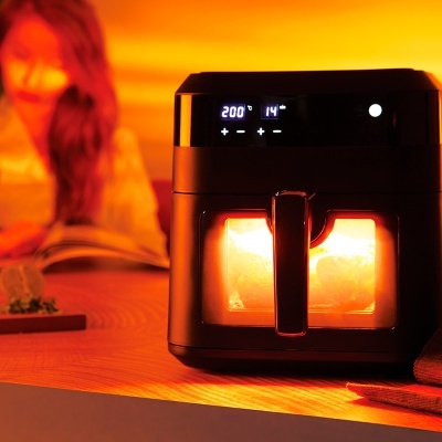 Fritadeira elétrica preta com visor digital e luz interior numa mesa de madeira com luz ambiente laranja
