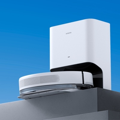 Robot aspirador branco com base de carregamento sobre superfície cinzenta e céu azul