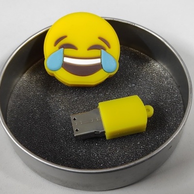Pen USB amarelo com emoticon sorridente em caixa metálica redonda.