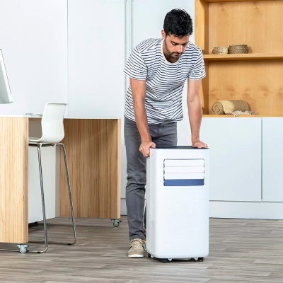 Homem move aparelho portátil branco numa sala com chão de madeira e móveis claros.