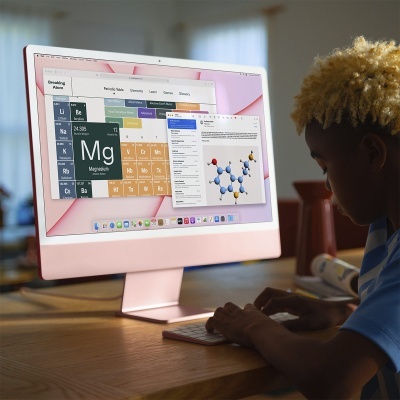 Computador de secretária rosa claro com ecrã grande a mostrar tabela periódica e molécula 3D usado por pessoa numa mesa de madeira