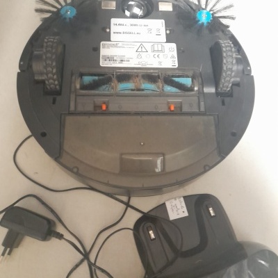 Robot aspirador circular preto com duas escovas laterais e base de carregamento preta