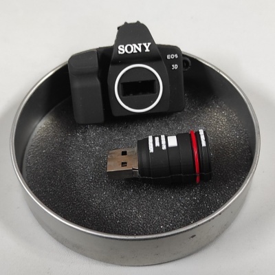 Pen USB em formato de máquina fotográfica digital Sony dentro de uma caixa metálica redonda com espuma preta