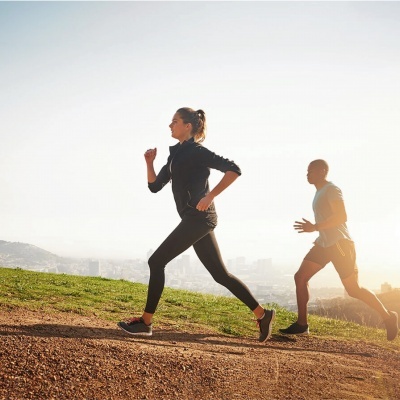 Duas pessoas a correr ao ar livre num trilho junto a área verde sob céu claro