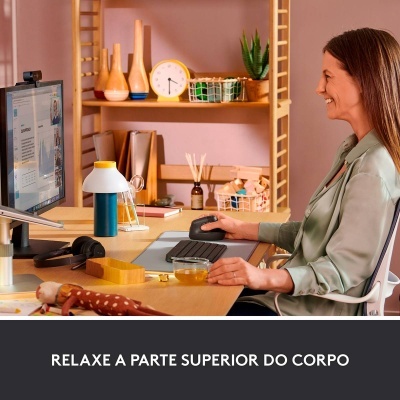 Mulher sentada a trabalhar num escritório em casa com objetos na secretária e estante ao fundo