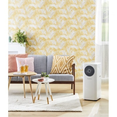 Sala com sofá cinza, mesas de centro, tapete claro, papel de parede amarelo com folhas e aparelho branco no chão