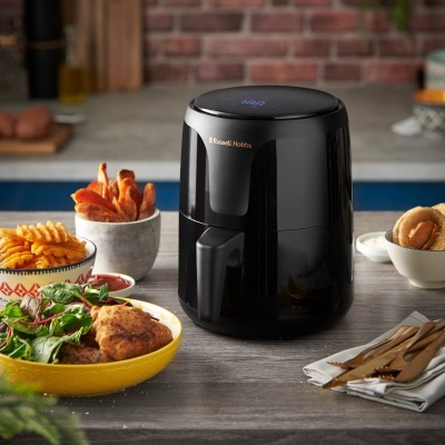 Frigideira elétrica preta Russell Hobbs com comida variada em pratos ao redor sobre mesa cinzenta