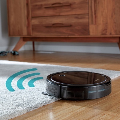 Aspirador robô preto a limpar chão de madeira junto a tapete cinza