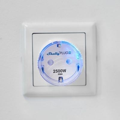 Tomada elétrica Shelly PLUG S com luz azul, 2500W max, numa parede branca