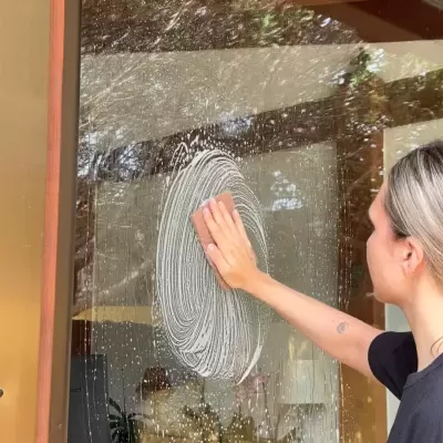 Pessoa a limpar porta de vidro com espuma branca em movimento circular