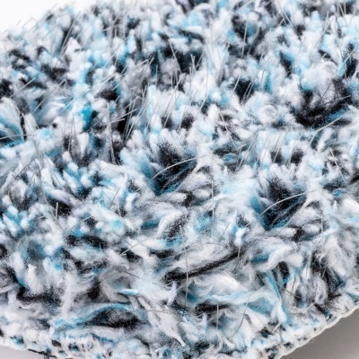 Close de tapete felpudo azul, branco e preto com textura densa e costura na borda.