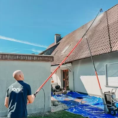 Homem usando máquina de alta pressão para limpar telhado usando lança telescópica laranja