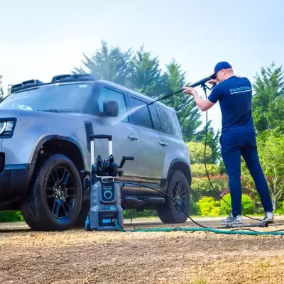 Homem a lavar SUV cinzento com máquina de lavar a alta pressão azul e cinza ao ar livre