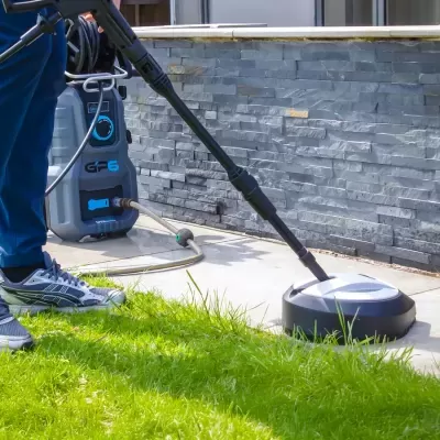 Máquina de alta pressão a limpar pavimento exterior junto a relva e parede