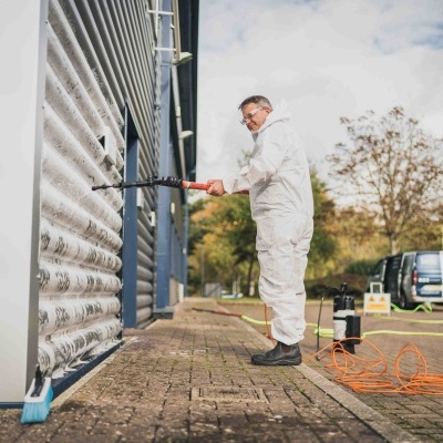 Homem com fato branco lava porta metálica com pistola de pressão