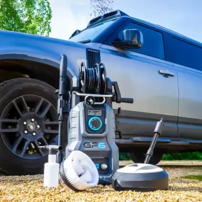 Equipamento de lavagem a pressão com acessórios em frente a SUV cinzento em pedra solta