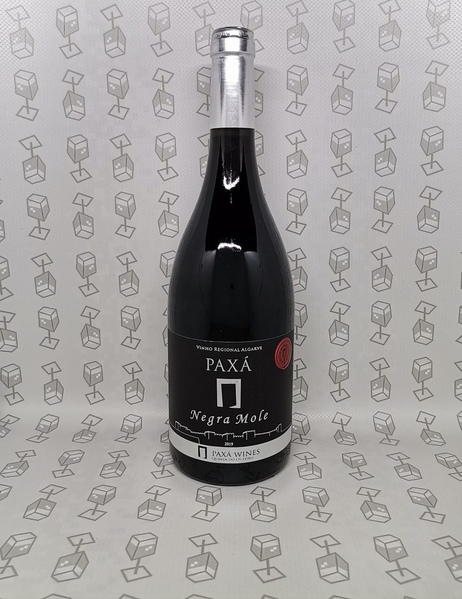 Garrafa de vinho tinto PAXÁ Negra Mole com rótulo preto e branco e fundo cinzento com padrão geométrico