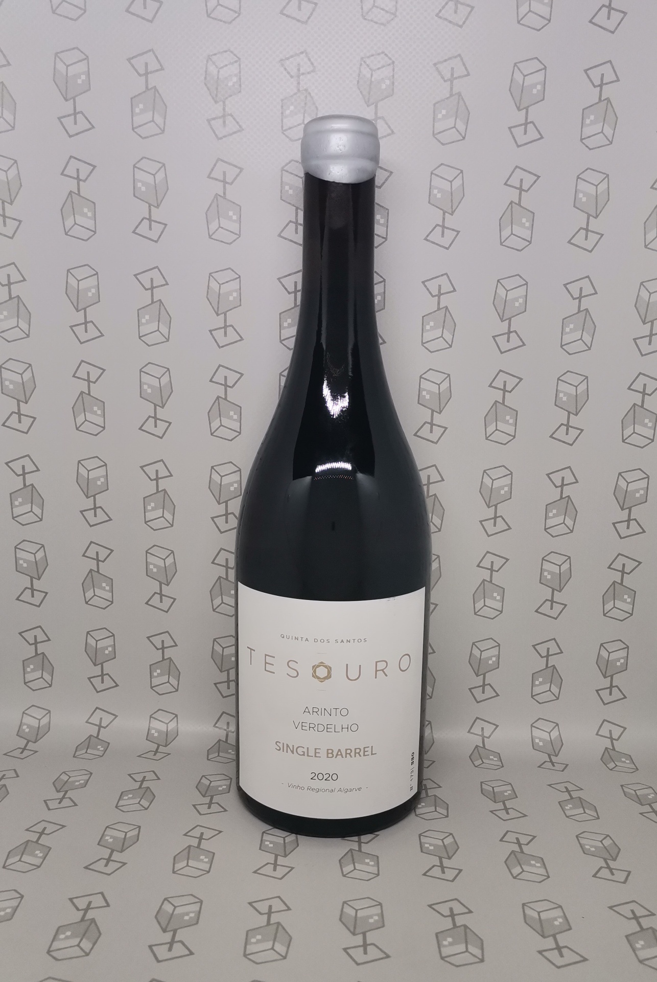 Garrafa de vinho TESOURO com rótulo branco e cápsula prateada sobre fundo com padrão de caixas de papelão.