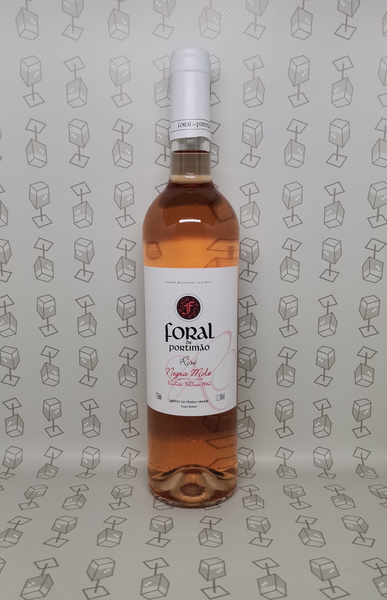 Garrafa de vinho rosé com rótulo branco e texto colorido, em fundo bege com padrão cinza