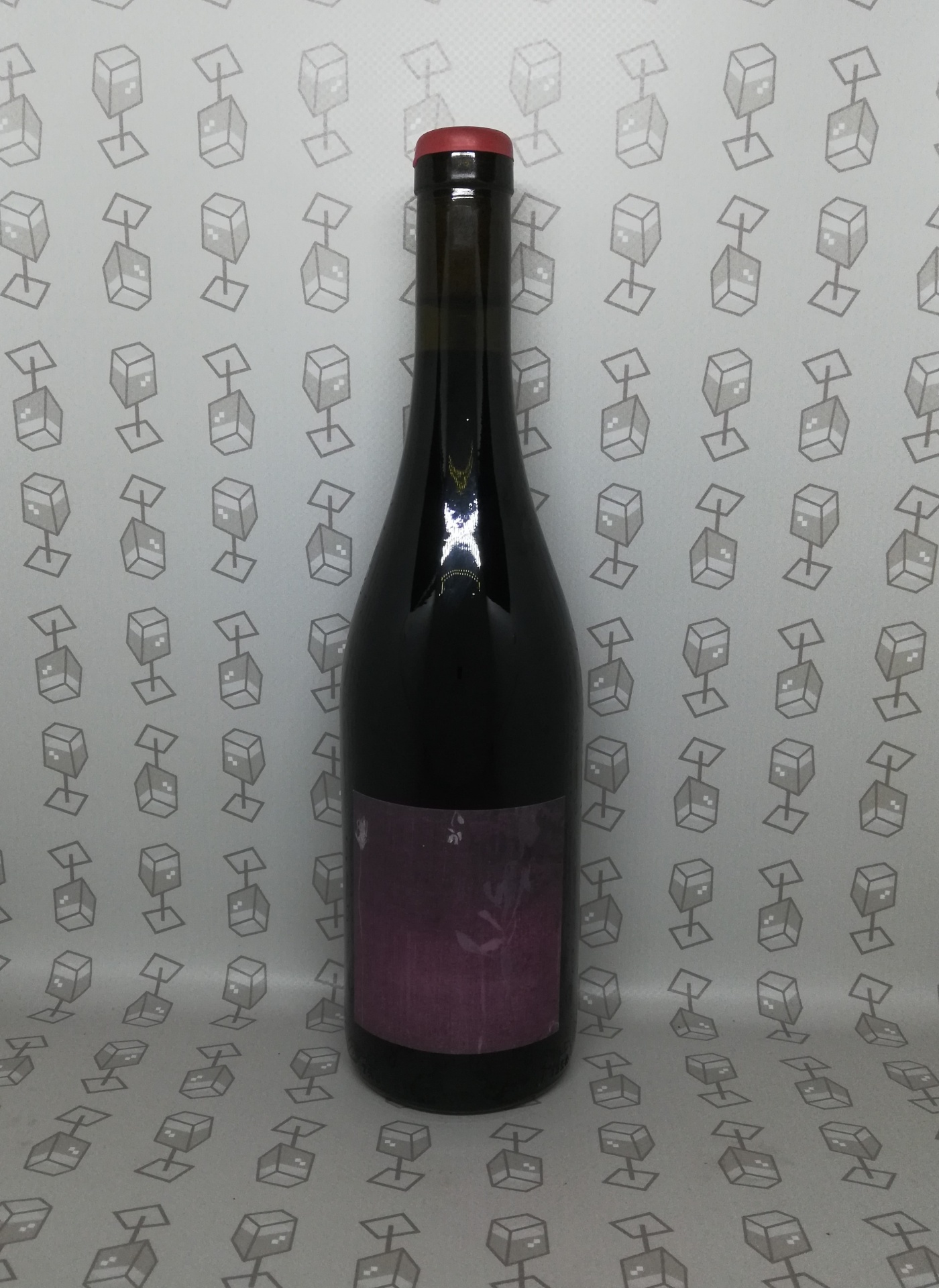 Garrafa de vidro escuro com rolha vermelha e rótulo roxo em fundo com padrão de cubos