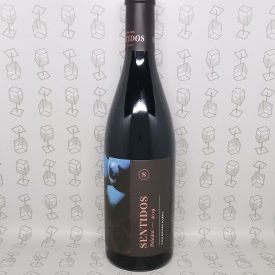 Garrafa de vinho tinto com rótulo castanho e rosa e fundo branco com padrão de cubos