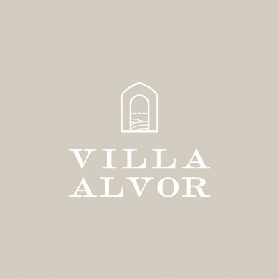 Logótipo VILLA ALVOR em branco sobre fundo bege claro com símbolo de janela/arco