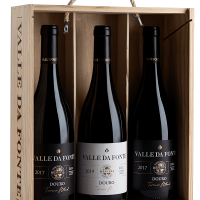 Caixa de madeira com três garrafas de vinho tinto Valle Da Fonte em fundo preto.