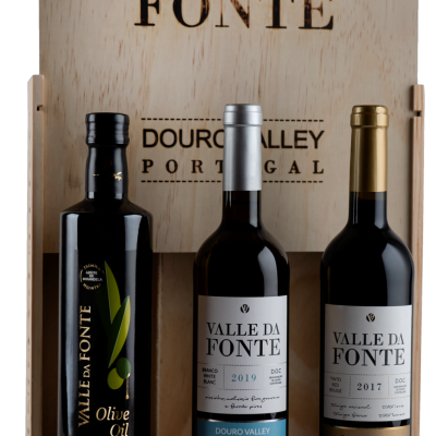 Três produtos Valle Da Fonte: azeite extra virgem e duas garrafas de vinho com rótulos azul e dourado em caixa de madeira.