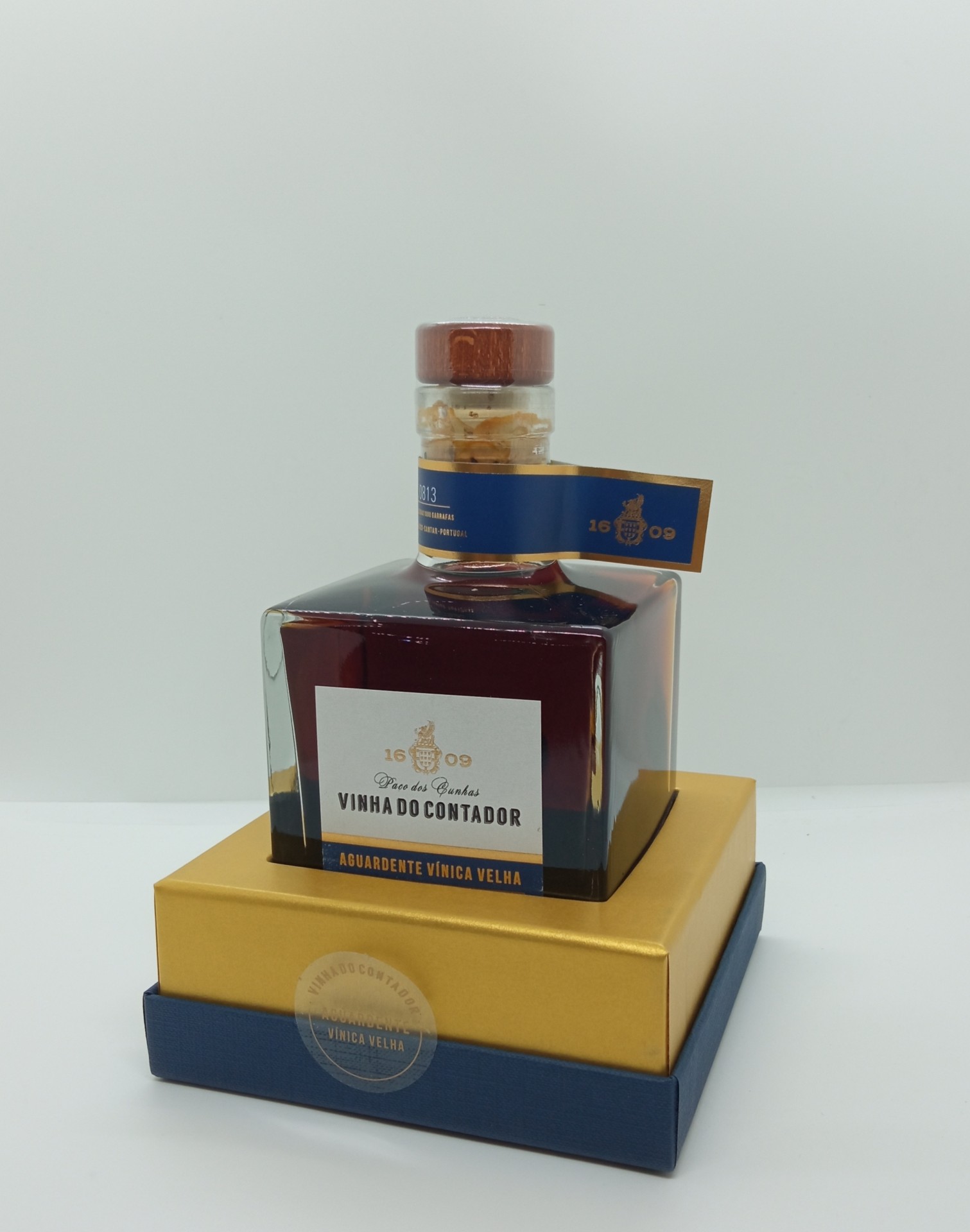 Garrafa quadrada de aguardente sobre caixas dourada e azul.
