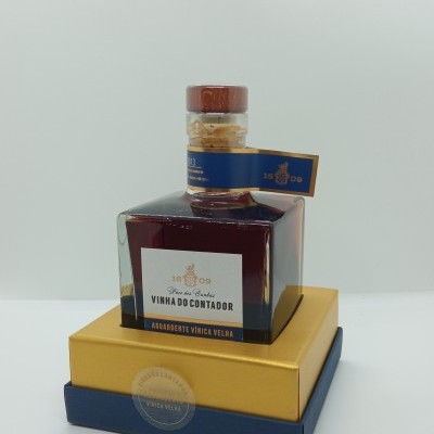 Garrafa quadrada de aguardente sobre caixas dourada e azul.