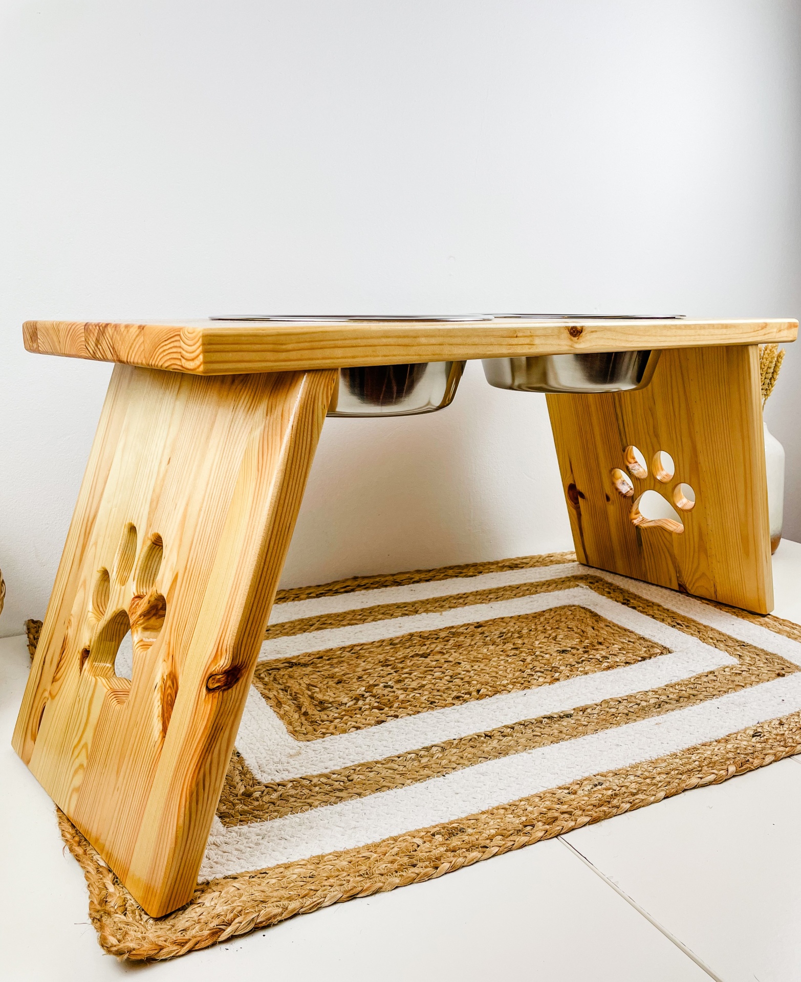 Tabuleiro Mellow Comedouro elevado em madeira com tigelas metálicas embutidas e recortes de pata nas laterais, sobre tapete bege e branco.