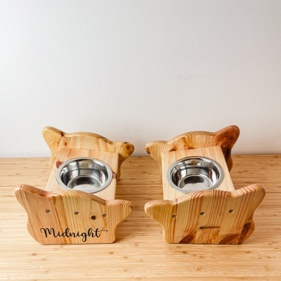 Dois comedouros em madeira com formas de cabeça de gato, com taças metálicas encaixadas, um com nome 'Midnight'