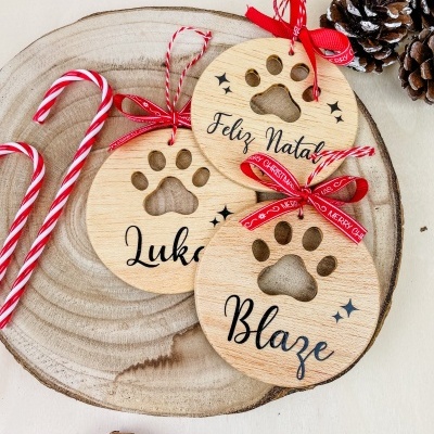 Três decorações redondas em madeira clara com recorte de pata e textos Natalinos em português.