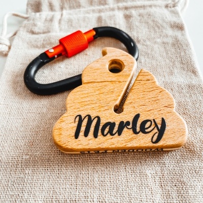 Chaveiro de madeira em formato de nuvem com texto 'Marley' e mosquetão preto com trava vermelha sobre saco de tecido.
