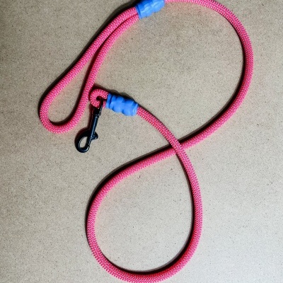 Trela de corda rosa com extremidades azuis e gancho metálico preto sobre fundo bege