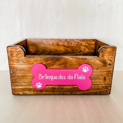Caixa de madeira castanha para brinquedos com placa rosa em forma de osso com texto e pegadas