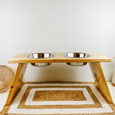 Comedouro elevado para animais com tigelas metálicas em madeira clara sobre tapete bege em interior