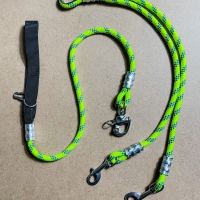 Três trelas para cães verdes neon com detalhes azuis e ganchos metálicos sobre fundo castanho claro.