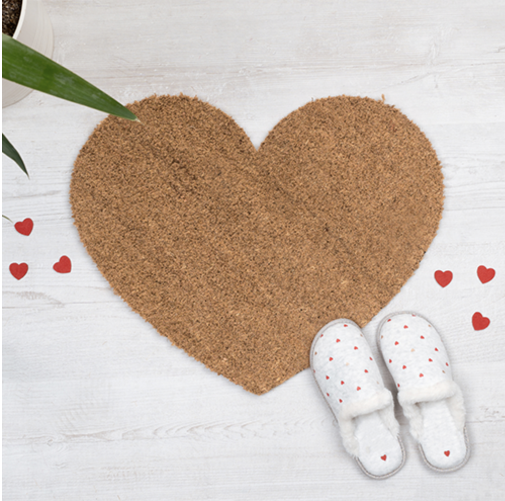 Tapete de entrada em formato de coração em fibras naturais com chinelos brancos de corações vermelhos sobre piso de madeira clara
