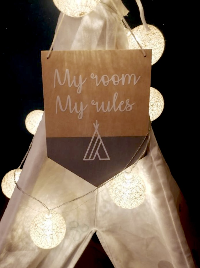 Painel decorativo em papel castanho pendurado num tecido branco semelhante a um tipi, iluminado por luzes brancas redondas.