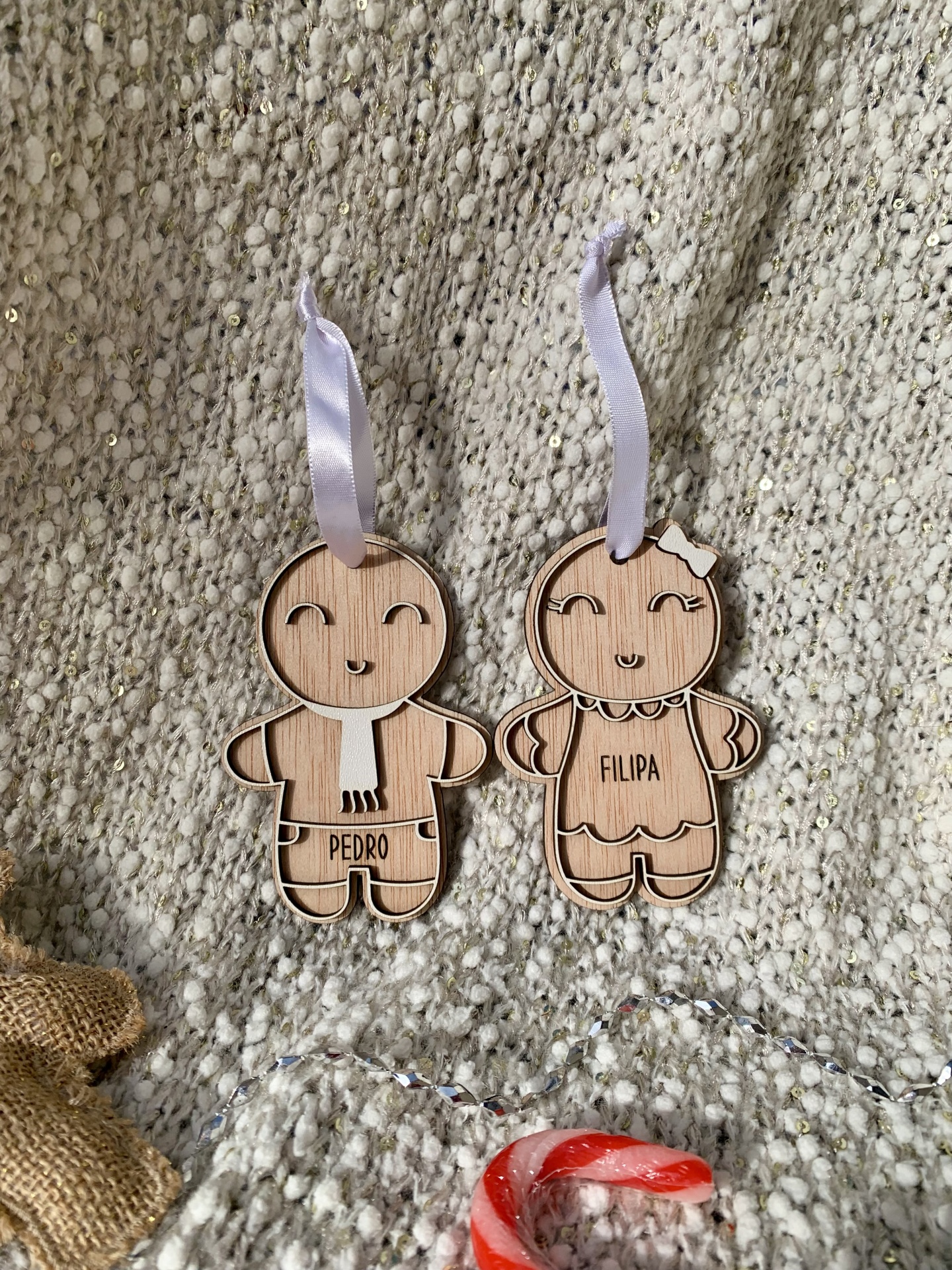Dois enfeites de madeira em forma de bonecos com nomes Pedro e Filipa pendurados em tecido texturizado bege