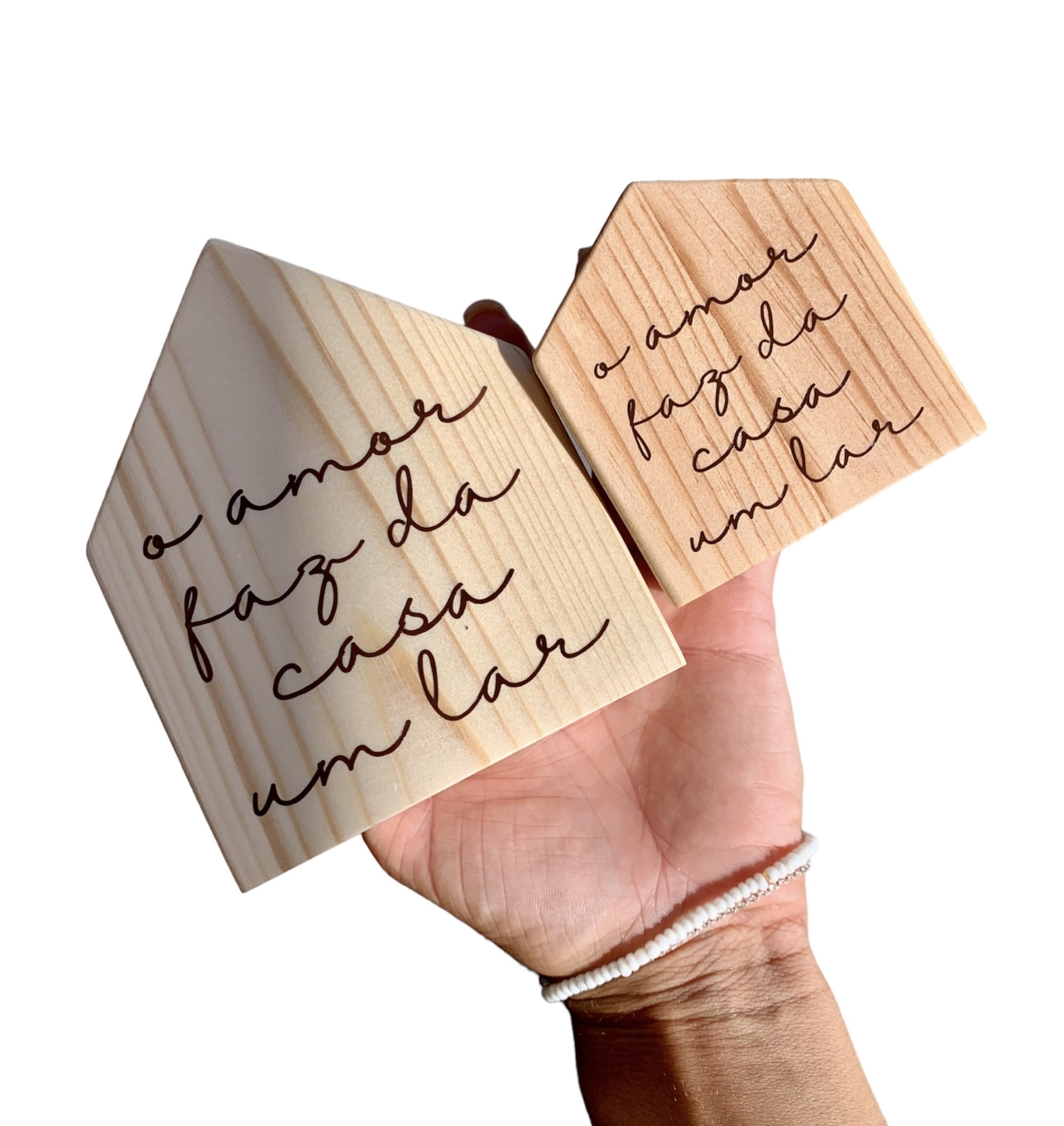 Objetos de madeira em forma de casa com gravação em português, segurados por mão.