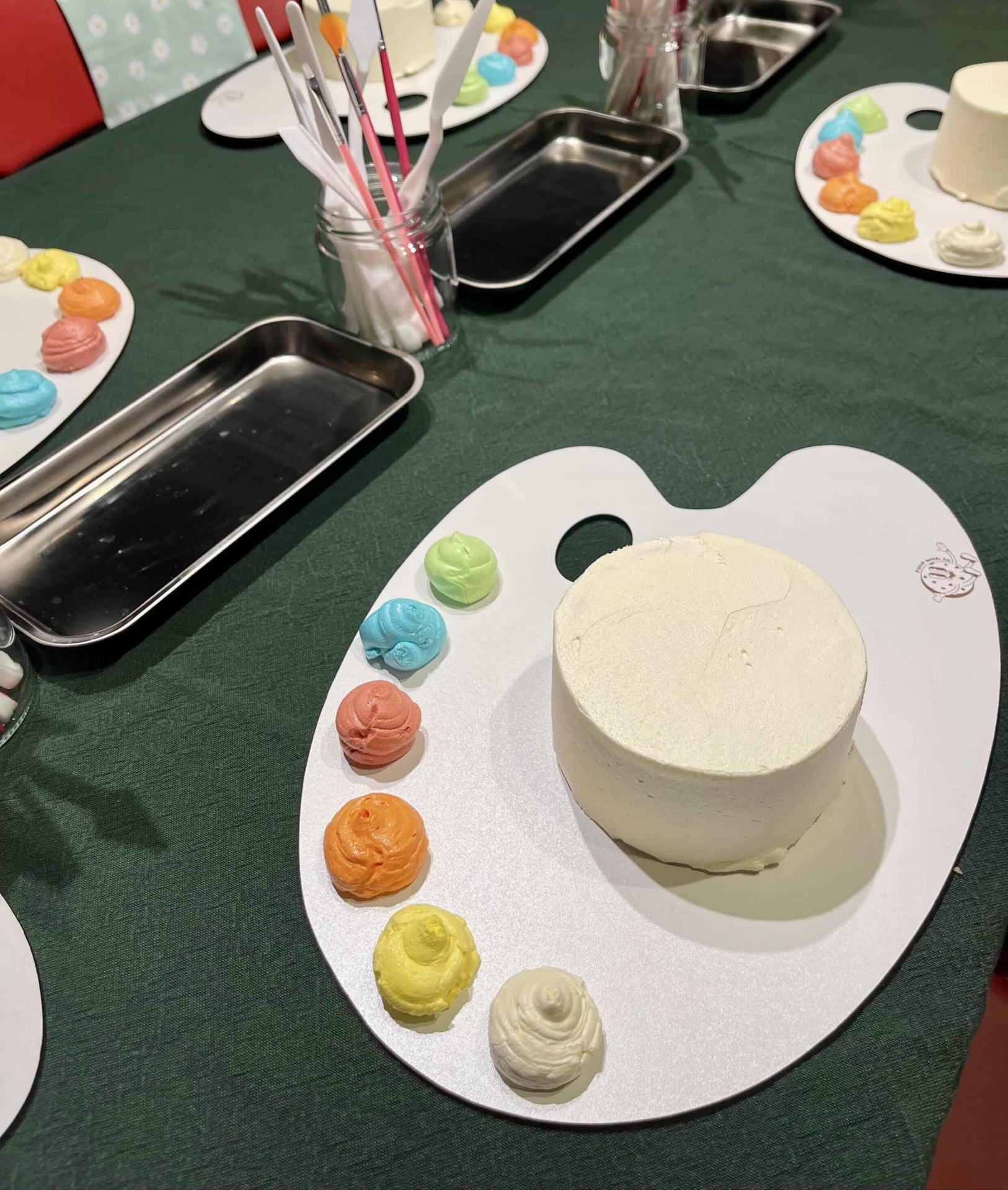 Bolo branco pequeno com várias cores de creme em paleta de pintura sobre mesa