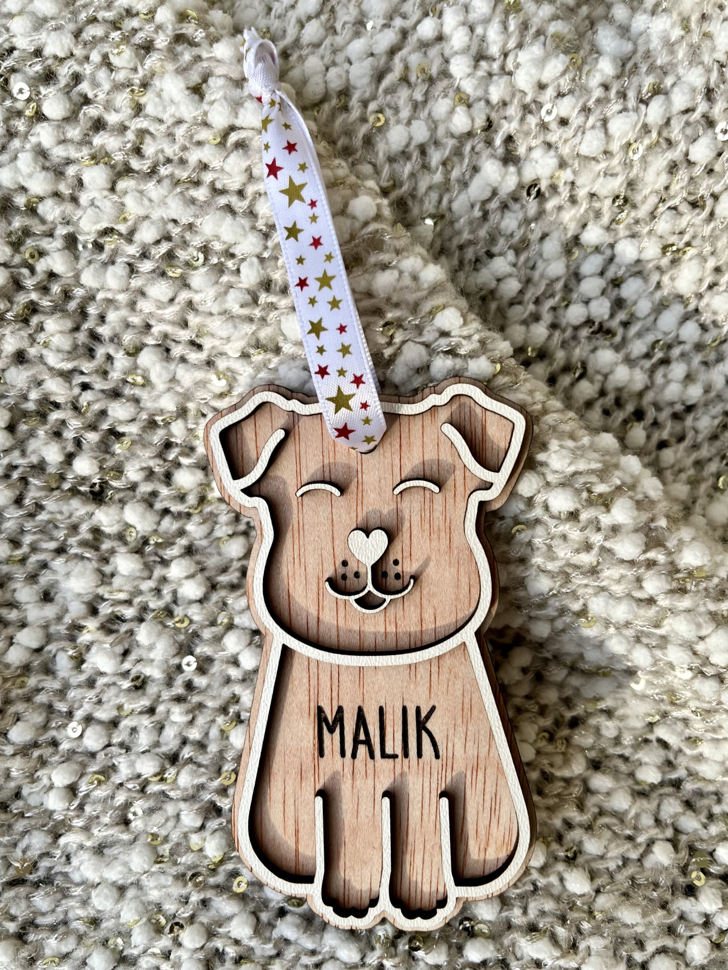 Enfeite de cachorro de madeira com a palavra MALIK e fita com estrelas sobre tecido felpudo
