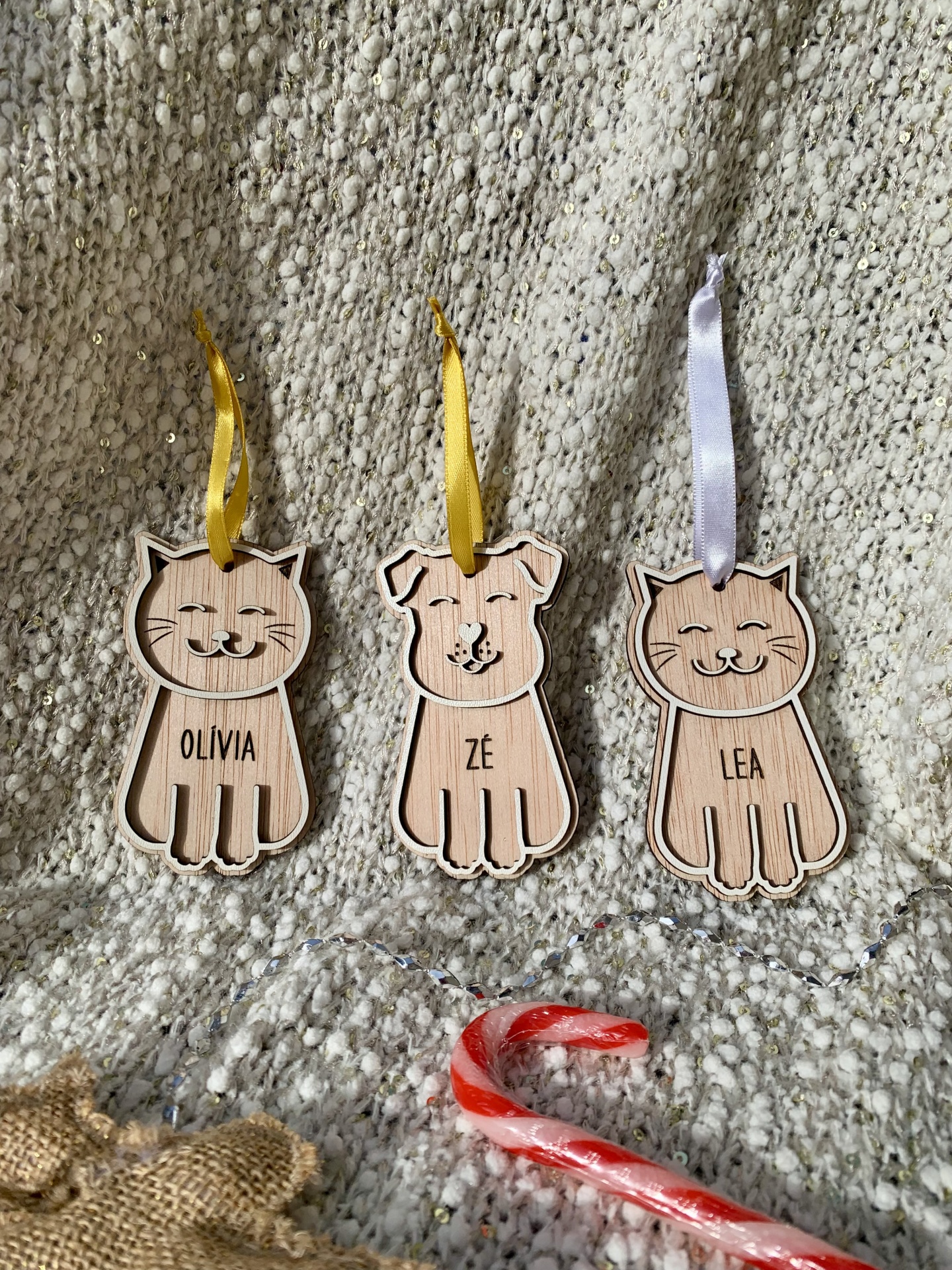 Ornamentos de madeira com formas de animais e fitas para pendurar sobre manta texturada