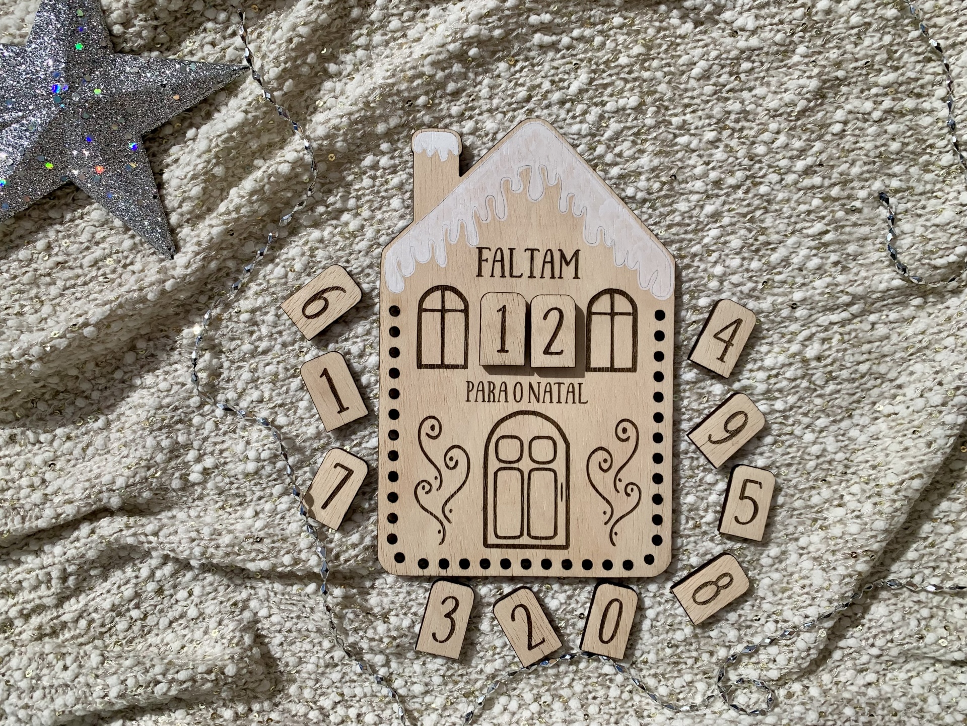 Contagem decrescente para o Natal em madeira com números destacáveis, em fundo de tecido cinzento brilhante.