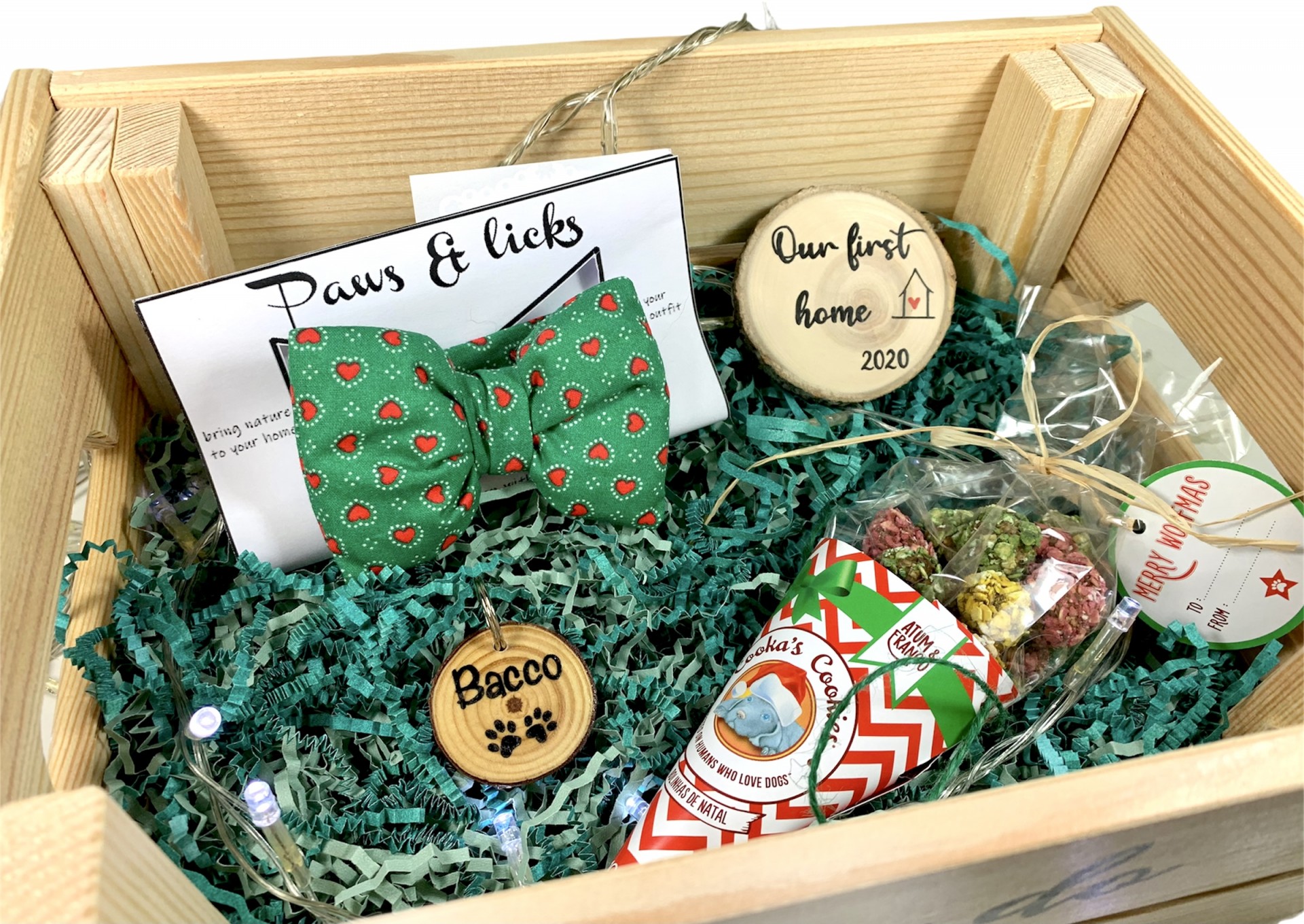 Caixa de presente com gravata borboleta verde com morangos, biscoitos decorativos com texto Our first home 2020 e Bacco, e petiscos para cães.