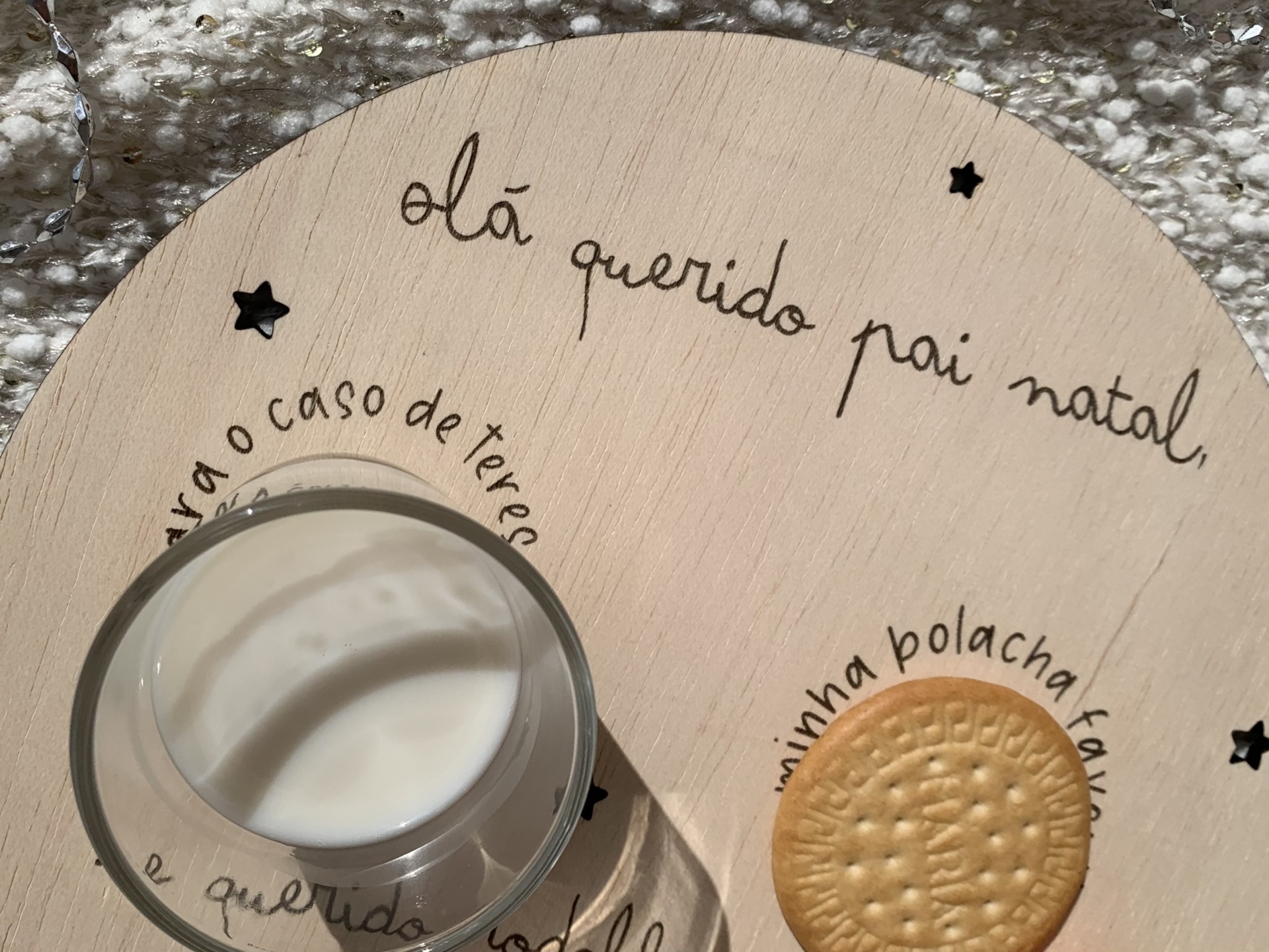 Prato redondo de madeira clara com copo de leite e bolacha, com texto em português e estrelas pretas