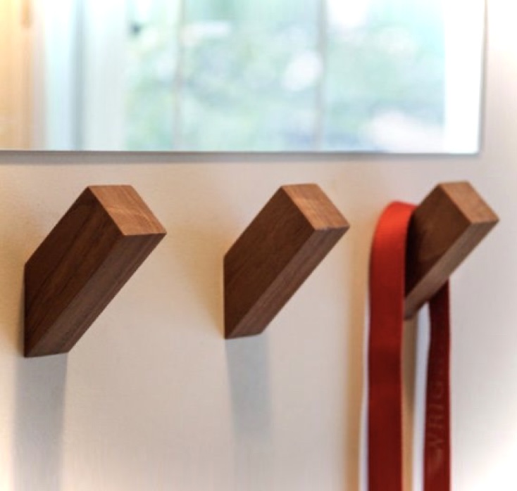 Três ganchos de parede em madeira com um cinto vermelho pendurado.